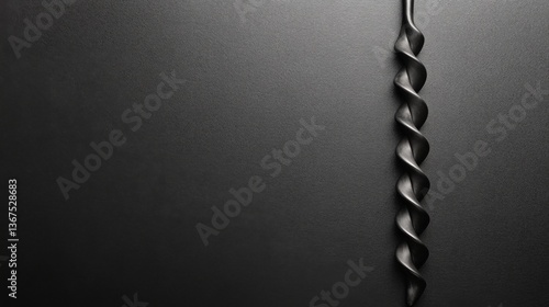 Twisted Black Drill Bit Against a Smooth Dark Textured Surface