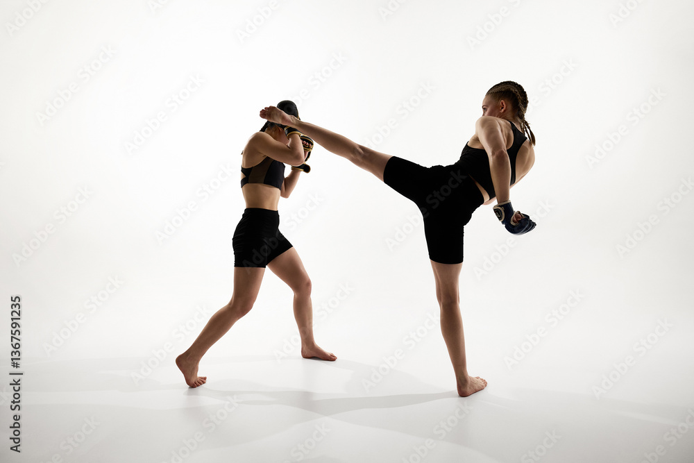 Strong female athletes in active stance, executing high kick and blocking punch during martial arts training against white background. Concept of sport, thai boxing, MMA, fight, strength, motion Strong female athletes in active stance, executing high kick and blocking punch during martial arts training against white background. Concept of sport, thai boxing, MMA, fight, strength, motion