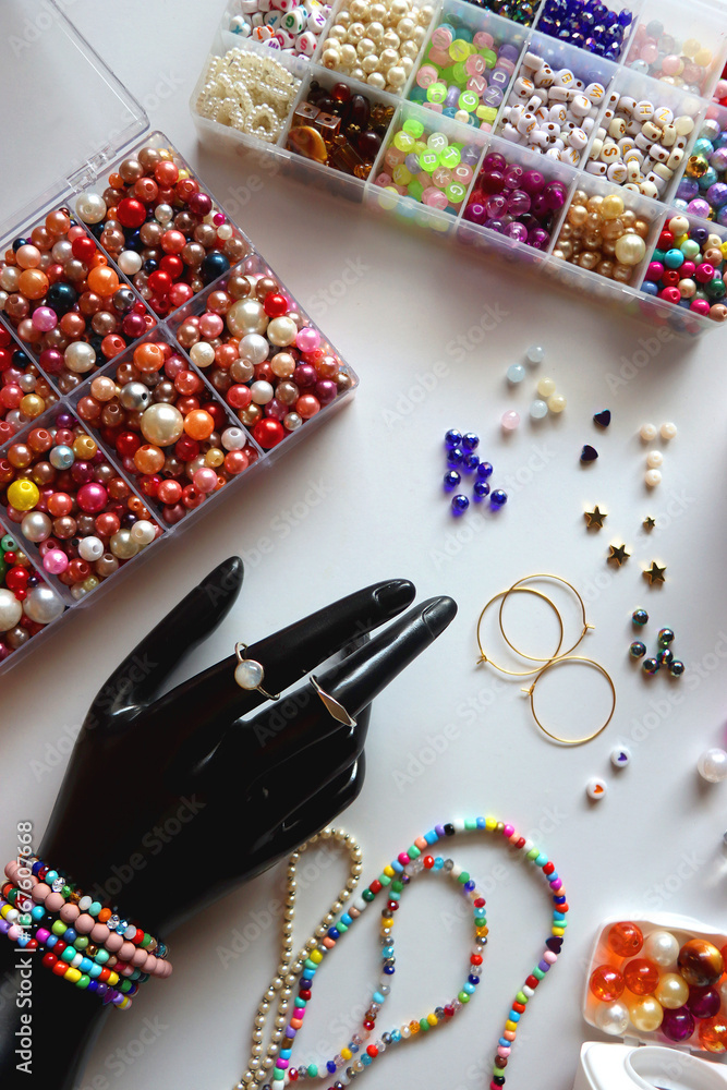 Hand figurine, colorful friendship bracelets, necklaces, various beads and DIY supplies on the table. Making jewelry at home. Flat lay.