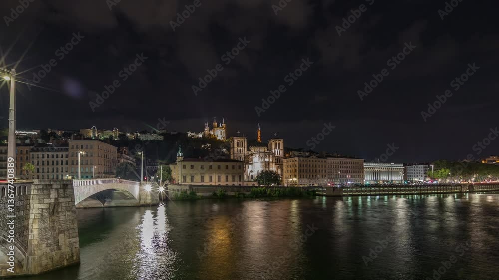 Panorama showing night timelapse of Lyon's cityscape with the red suspension footbridge over the Saone River, Saint John the Baptist Cathedral and Notre-Dame. Illuminated waterfront in the evening Panorama showing night timelapse of Lyon's cityscape with the red suspension footbridge over the Saone River, Saint John the Baptist Cathedral and Notre-Dame. Illuminated waterfront in the evening