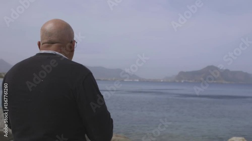 Uomo di spalle, beve birra su una spiaggia mentre guarda il mare.