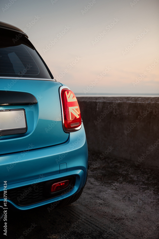 Naklejka premium Blue compact car at dusk. Rear part of hatchback in parking lot, close-up view of the right rear tail light. 