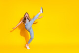 Cheerful young woman in casual attire joyfully kicking on a vibrant yellow background showcasing energy and happiness