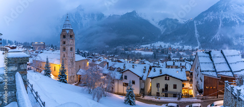 View of Church of Saint Pantalon and the snow covered town centre and mountainous background in winter, Courmayeur, Aosta Valley