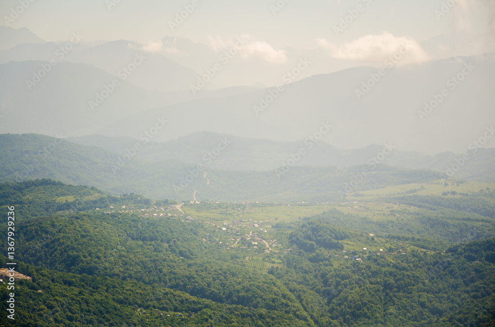 Naklejka premium Expansive view of lush, green mountains under clear blue sky. Rolling hills and valleys stretch into distance, enveloped in soft daylight. Small villages nestled in verdant scenery