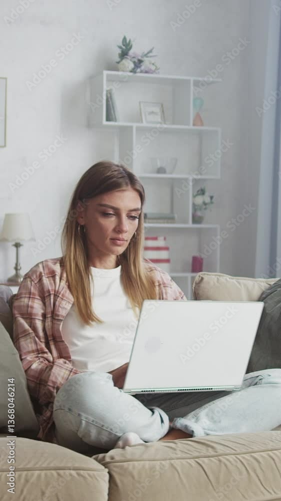 Young woman sitting on a comfortable sofa in a cozy living room, working remotely with a laptop. The scene captures a relaxed atmosphere, showcasing productivity and focus in a modern home setting Young woman sitting on a comfortable sofa in a cozy living room, working remotely with a laptop. The scene captures a relaxed atmosphere, showcasing productivity and focus in a modern home setting