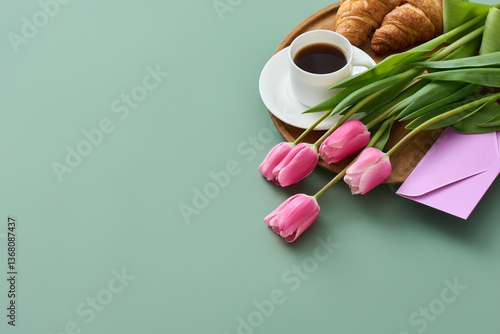 A cozy breakfast in bed for Mother's Day. A tray holds fresh pink tulips, warm croissants, a cup of coffee, and a sentimental greeting card.