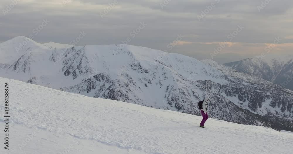 Lone hiker glides down wide snow covered slope under a vast open sky with mountain ridges and sunlight diffused through clouds Lone hiker glides down wide snow covered slope under a vast open sky with mountain ridges and sunlight diffused through clouds