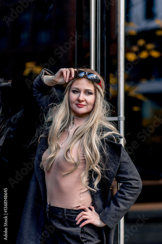 Obraz na płótnie Portrait of blonde stylish woman posing near glass doors wearing black pants and coat w salonie