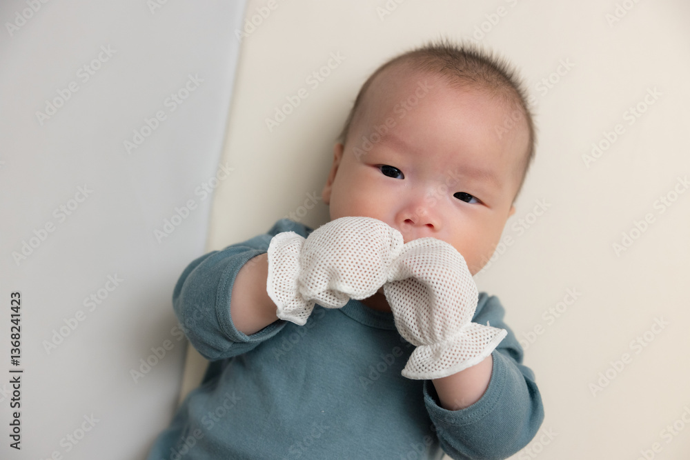 Sweet newborn baby wearing glove sucking hand
