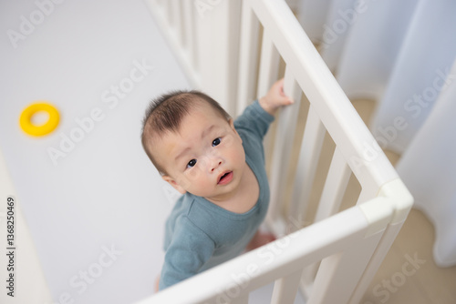 Little baby standing in playpen holding railing