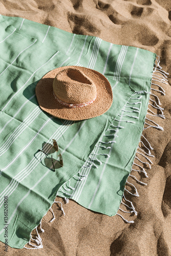 Fototapeta Naklejka Na Ścianę i Meble -  Green towel, straw hat, sunglasses on beach sand background. Aesthetic lifestyle, summer vacation concept. Sunbathing, beach party, holiday picnic. Travel fashionable blog, social media, top view.