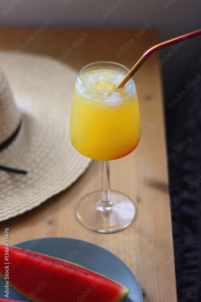 Plate with watermelon slices, glass of orange juice or cocktail, straw hat, colorful beaded necklace and sunglasses on the wooden table. Summer essentials concept. Selective focus.