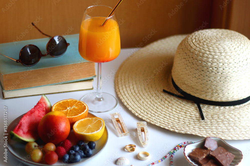 Glass of cocktail, straw hat, sunglasses, books, fresh fruit, chocolate and accessories. Summer essentials on the table. Selective focus.