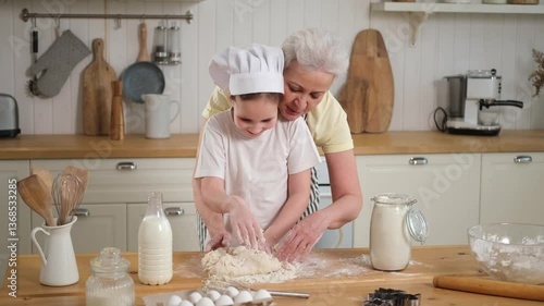 Happy family in kitchen. Grandmother and granddaughter child cook in kitchen together. Grandma teaching kid girl knead dough bake cookies. Household teamwork helping family generations concept