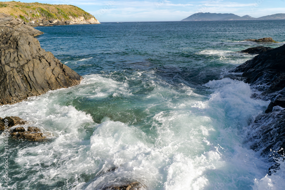 View of part of Praia do Forte, with many rocks and strong waves all over the beach, mountains in the background. Cabo Frio, Rio de Janeiro, Brazil. View of part of Praia do Forte, with many rocks and strong waves all over the beach, mountains in the background. Cabo Frio, Rio de Janeiro, Brazil.