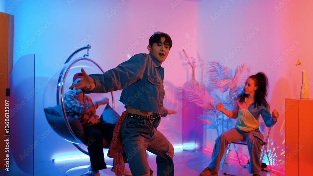 Fototapeta premium Skilled asian dancer moving to modern music while multicultural friend sitting at chair. Professional performer dancing show energetic foot step while hipster team cheering and supporting. Regalement.