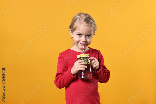 Girl drinking tasty cucumber water on orange background. Refreshing drink