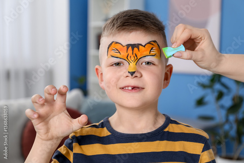 Animator drawing tiger on boy's face indoors, closeup