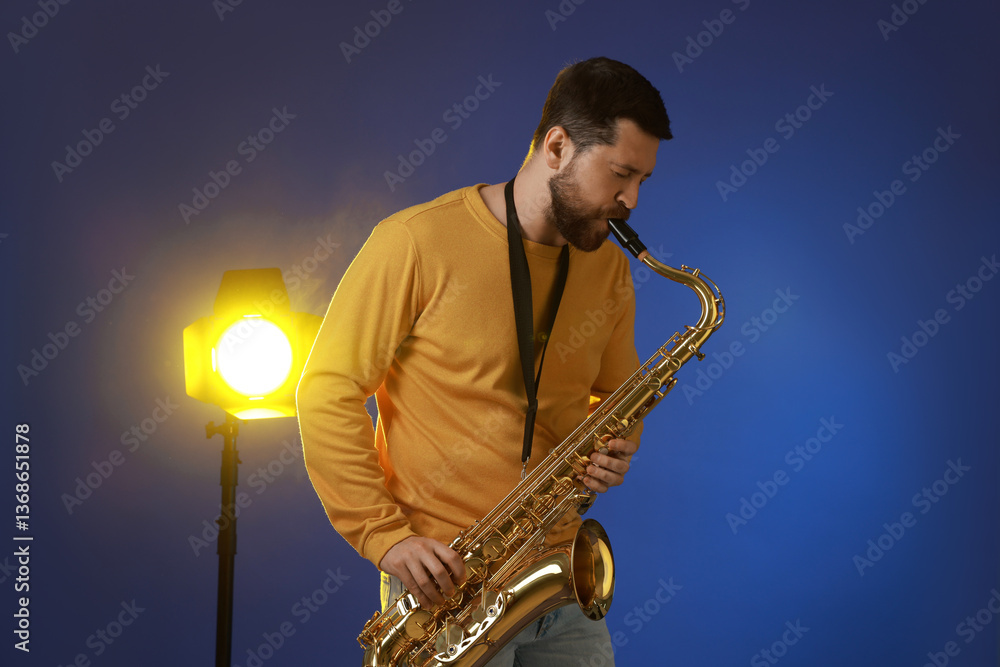 Fototapeta premium Professional musician playing saxophone on blue background with light
