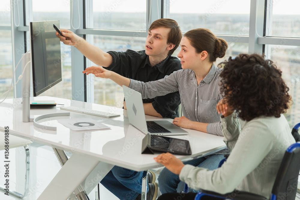 Obraz premium Teamwork brainstorm. Diverse multiracial colleagues woman in chair for people with disability working together. Group of people sitting in creative office discussing business. Young professional team