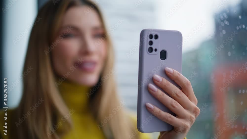 Blonde watching cellphone social media standing by apartment window closeup. Blonde watching cellphone social media standing by apartment window closeup.