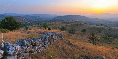 A serene sunset landscape with rolling hills and a stone wall in the foreground.
