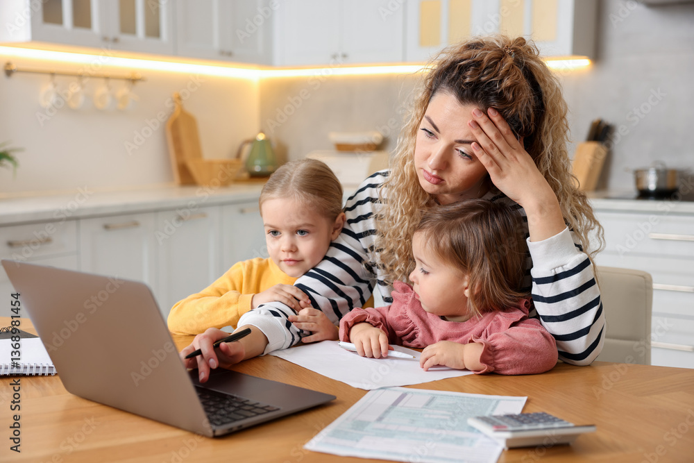 Single mother working on laptop and her daughters at table in kitchen Single mother working on laptop and her daughters at table in kitchen
