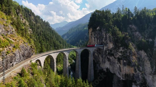 Drone footage of a train emerging from a tunnel and crossing the iconic Landwasser Viaduct in the Swiss Alps photo