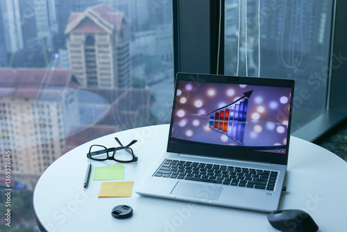 A professional office setting featuring a laptop on the office table, with the screen displaying a graph, representing business growth and data analysis.  Office buildings in the background.