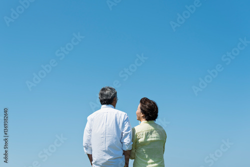 青空の下で寄り添い合うシニア夫婦