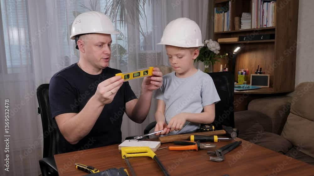 A caring attentive father shows his little son various tools while sitting at the table at home. The father teaches the son. A caring attentive father shows his little son various tools while sitting at the table at home. The father teaches the son.
