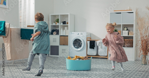 Happy siblings are fooling around in the laundry area, wrapped in warm sweatshirts fresh from the dryer, running between the clothes bowl and the bathroom washing machine.