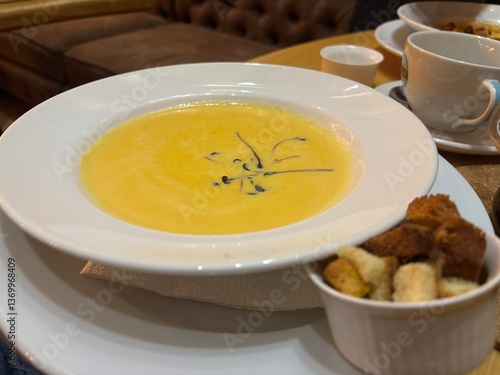 yellow cream soup in a white plate on the table in the restaurant is served for the guest