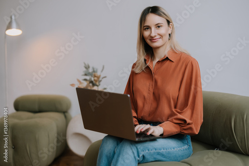 Young woman working on a laptop while sitting on a green couch in a modern living room during the day