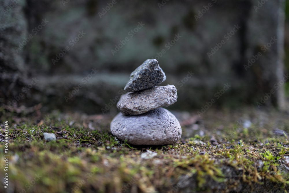 Small stack of three balanced stones on a moss-covered surface captured in a macro shot with a blurred background creating a tranquil and meditative atmosphere