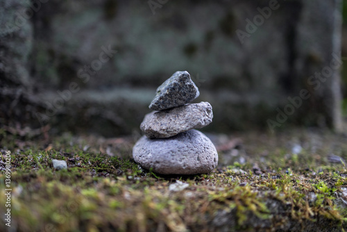 Obraz na płótnie Small stack of three balanced stones on a moss-covered surface captured in a macro shot with a blurred background creating a tranquil and meditative atmosphere w salonie