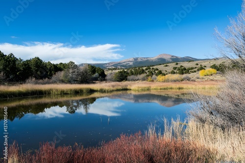 Serene mountain lake reflects sky. Autumn colors foreground. Crisp