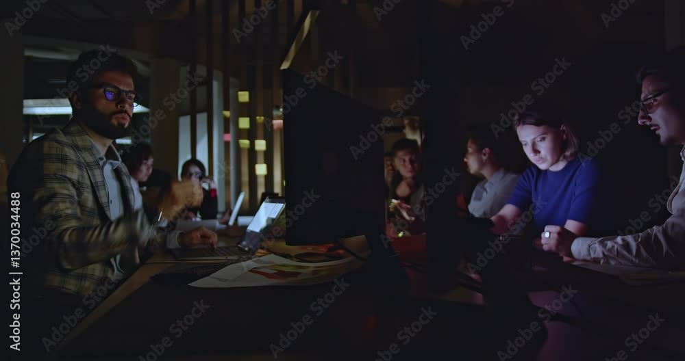 Business team working late in office, focused on computers and documents under dim lights. Pressure to meet deadline, intense atmosphere. Business team working late in office, focused on computers and documents under dim lights. Pressure to meet deadline, intense atmosphere.
