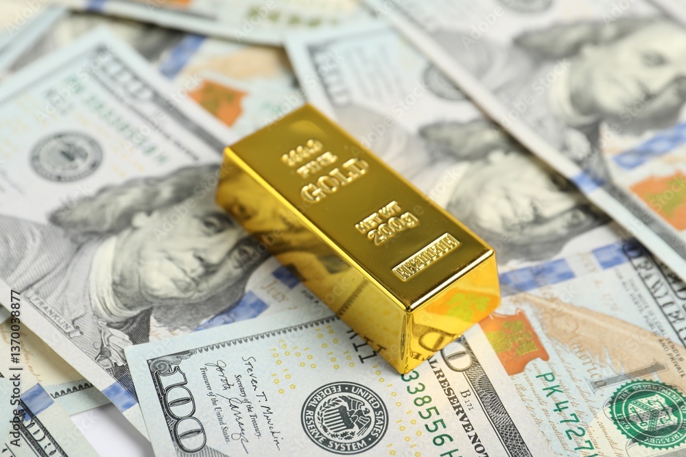 One shiny gold bar on dollar banknotes, closeup One shiny gold bar on dollar banknotes, closeup