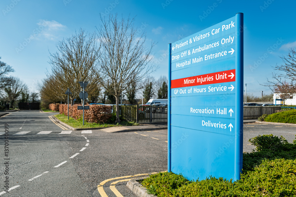 Large blue patient and visitor information and parking sign seen within the campus of a typical NHS hospital in Britain. The red sign is for the Minor Injury department.