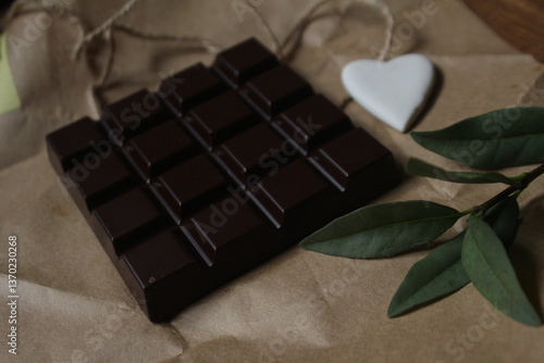 square dark chocolate bar displayed on brown craft paper with green leaves decor and white heart ornament