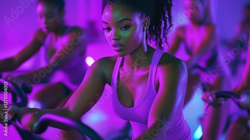 A woman focuses intently during a spin class illuminated by vibrant purple lighting.