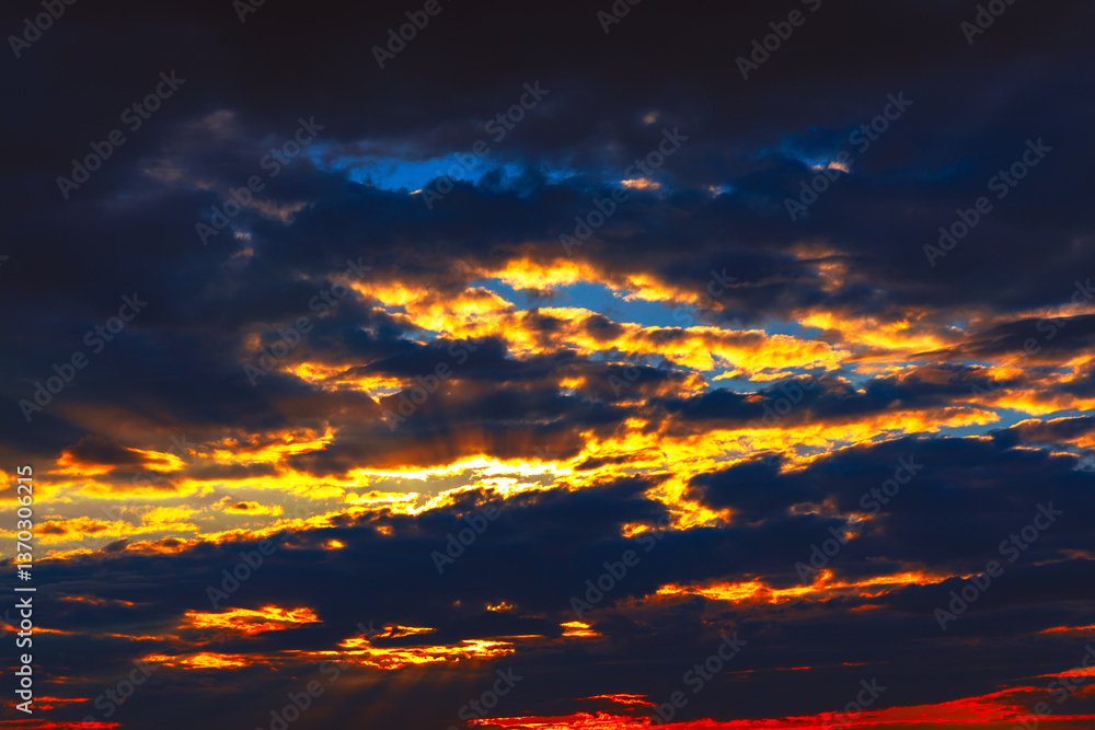 Dramatic sunset cloudscapes, vibrant hues of orange and gold against a dark backdrop. Fiery sunset, with intense colors piercing through the stormy clouds