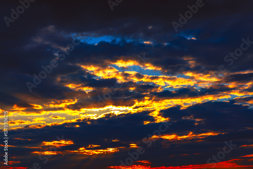 Obraz na płótnie Dramatic sunset cloudscapes, vibrant hues of orange and gold against a dark backdrop. Fiery sunset, with intense colors piercing through the stormy clouds w salonie