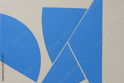 set of blue paper shapes machine-cut with linear and curved edges and arranged somewhat abstractly on beige paper
