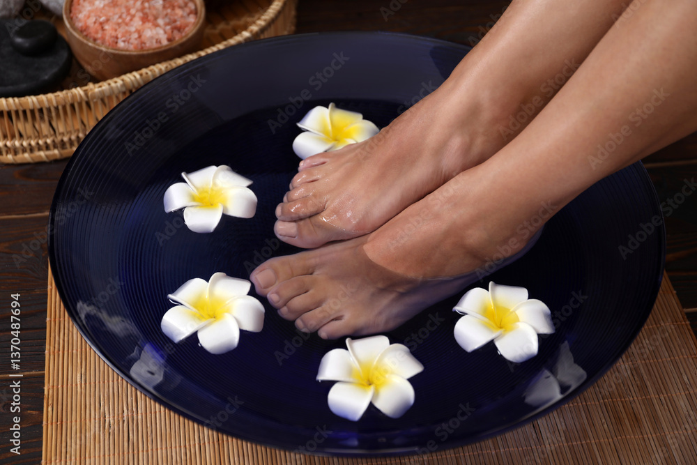 Woman soaking her feet in bowl with water and plumeria flowers on floor, closeup. Spa treatment Woman soaking her feet in bowl with water and plumeria flowers on floor, closeup. Spa treatment