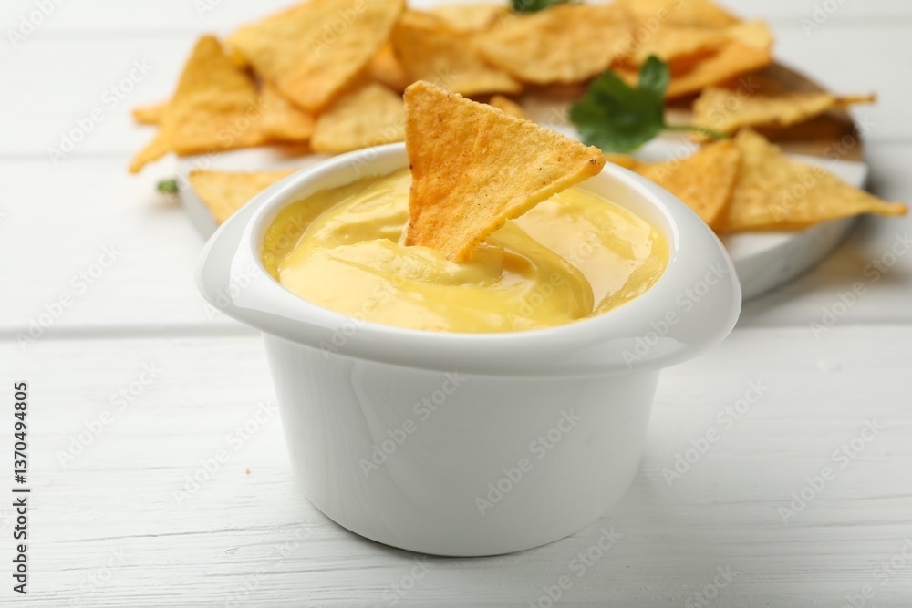 Tasty dipping cheese sauce in bowl and nacho chips on white wooden table, closeup Tasty dipping cheese sauce in bowl and nacho chips on white wooden table, closeup