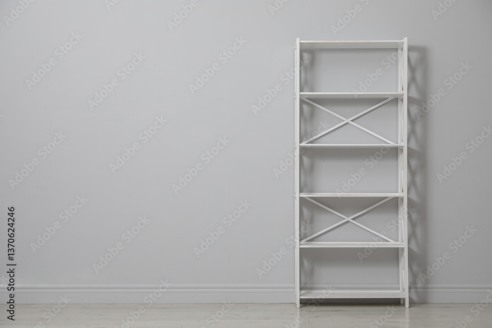 Empty shelving unit near light grey wall. Space for text Empty shelving unit near light grey wall. Space for text