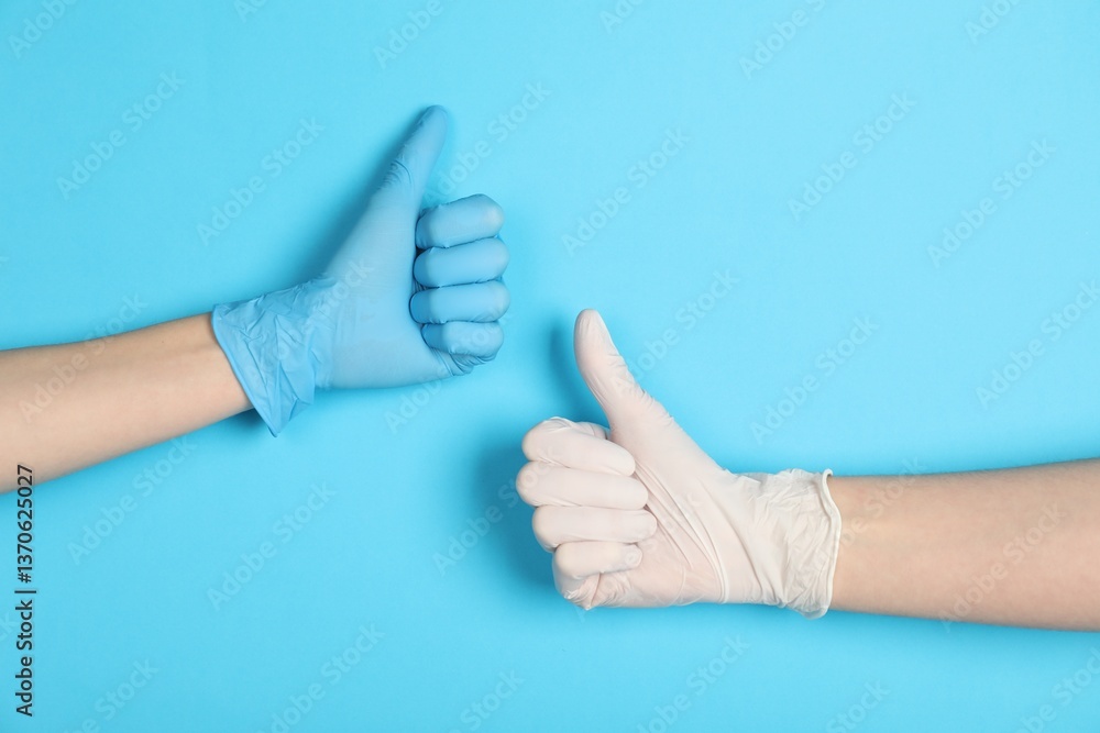 Doctors in medical gloves showing thumbs up on light blue background, closeup Doctors in medical gloves showing thumbs up on light blue background, closeup